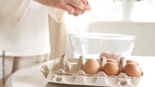 Woman is cracking eggs into a bowl. There are six eggs in the bowl