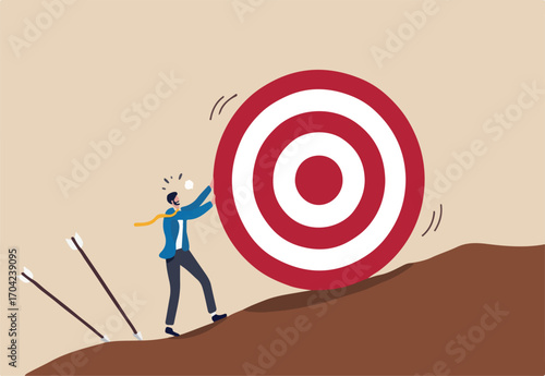 Missed target, failure or obstacle, difficulty in work that hard to achieve target or set too high or unrealistic goal concept, businessman trying hard to push dartboard or arrow target up the hill. 