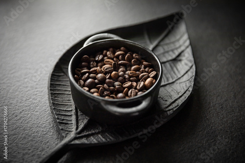 Ziarna kawy w miseczce na tle ozdobnej tacy w kształcie liścia Coffee beans in a bowl on a decorative leaf-shaped tray