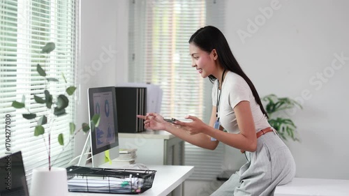 Professional businesswoman comparing business data on computer and smartphone, working efficiently in bright, contemporary office environment