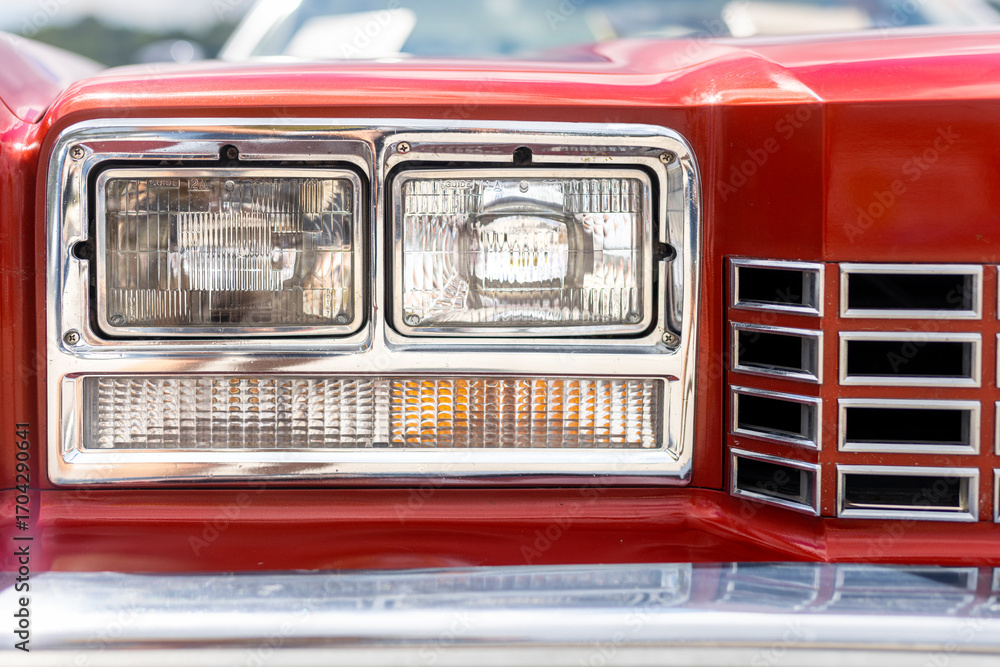 Fototapeta premium Detail of the red front hood with the light of an American retro car. Mask of an classic old hystory veteran