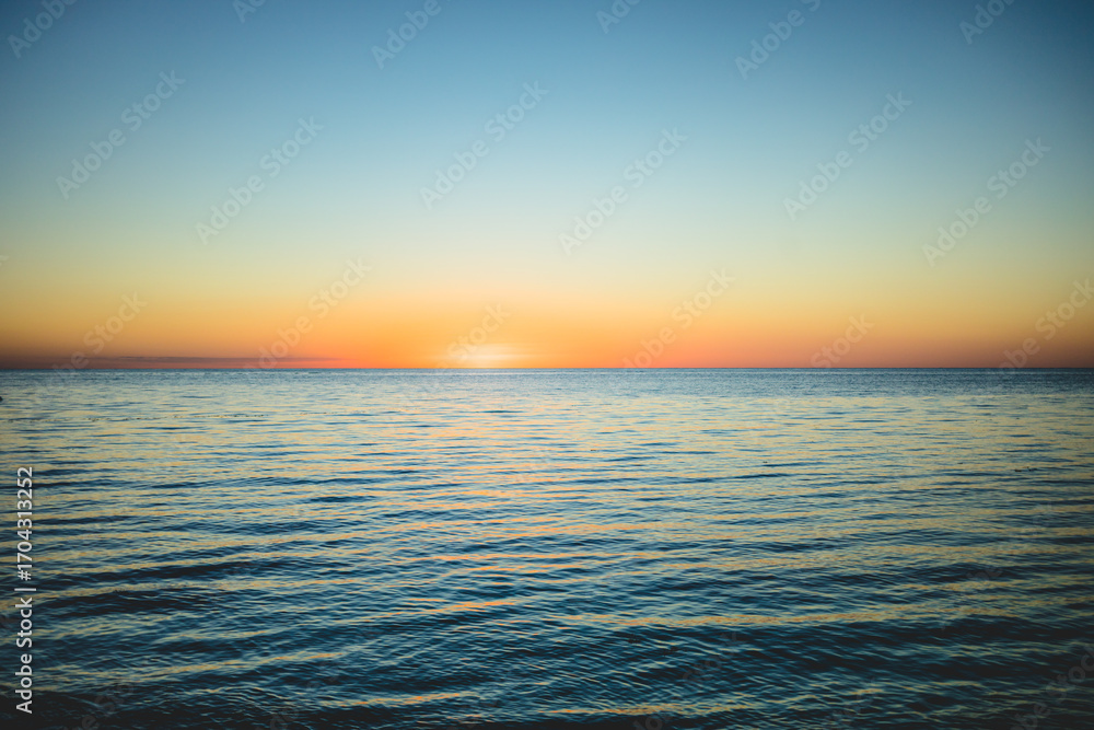 Obraz premium Vibrant sunset over tranquil ocean waters creates peaceful evening atmosphere