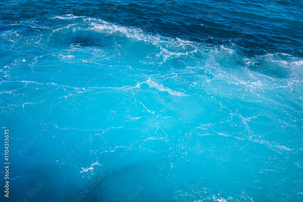 Fototapeta premium Vibrant turquoise waves gently rolling in under bright sunlight at a coastal location