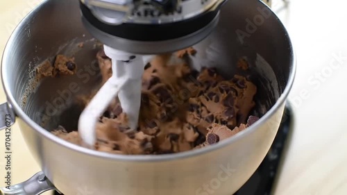A stand mixer with cookie dough and chocolate chips, solid cream background
