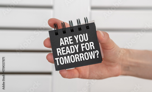 A hand holding a black spiral bound notebook with the words Are You Ready for Tomorrow
