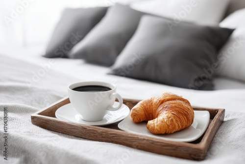 Breakfast on a hotel bed. Classic breakfast in bed on a wooden tray with coffee and croissants. Cozy morning scene. Blurred pillows in the background. Relaxing atmosphere. Warm bed breakfast setting