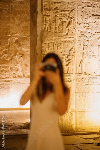 Mujer fotografiando templos egipcios con jeroglíficos antiguos iluminados
