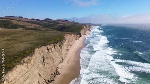 Aerial video of a cliff coastline in California with wild waves and a blue sky.