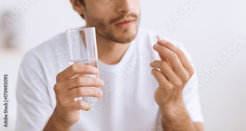 фотографія Pensive millennial european man hold glass of water and look at pill in hand, close up