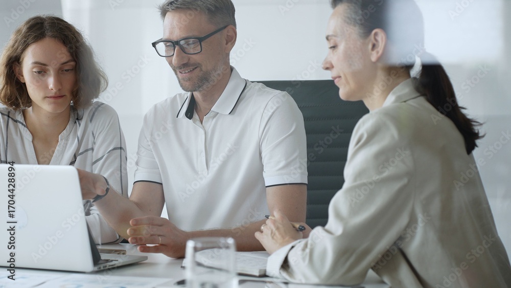 Fototapeta premium Professional team working together, reviewing digital analytics on laptop screen while strategizing corporate project details in modern workplace environment. Business people concept