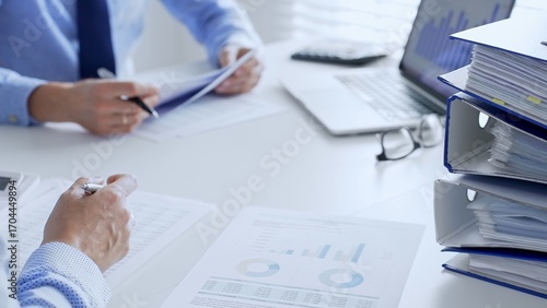 Accountants are analyzing financial reports with magnifying glass and documents, performing accounting and auditing tasks in the office, close up. Audit and taxes in business