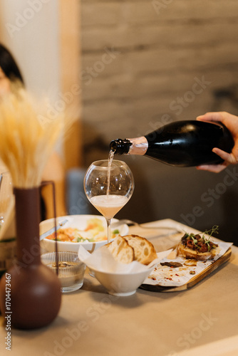 Wallpaper Mural Pouring sparkling wine into a glass during cozy dinner with gourmet appetizers Torontodigital.ca