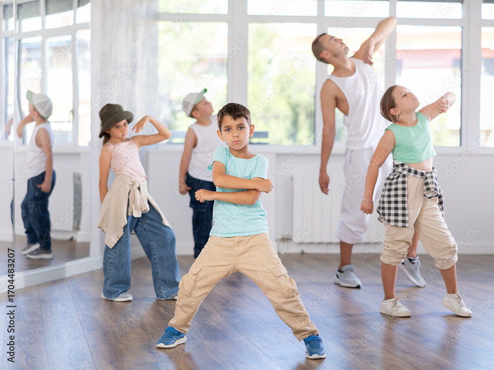 Naklejka premium In sports studio, creative childrens team learns hip-hop dance accompanied by experienced man teacher