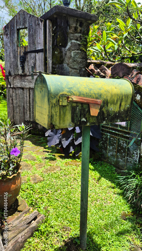 Photo of an old green metal mailbox mounted on a post in a garden.