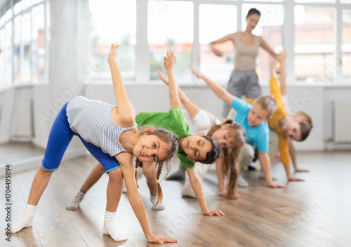 Children perform bends, stretches and squats to prepare their muscles and body. Students participate in physical education lesson, prepare for dance lesson.