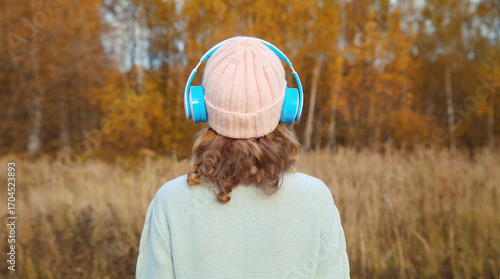 Inspired young woman enjoying listening to music in headphones outdoors in autumn forest