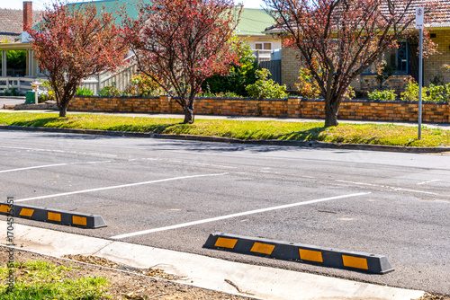 Wheel stops in marked parking bays on suburban residential street in Melbourne, Australia, with pedestrian sidewalk and houses in the background. Concept of parking safety, urban infrastructure