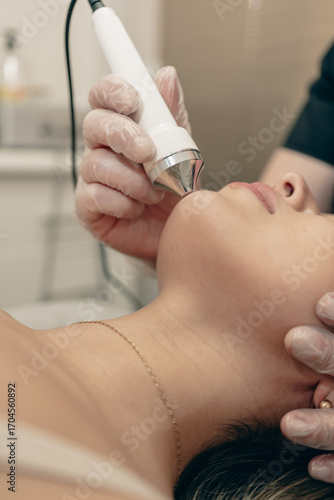 Close up of physiotherapist woman performing facial treatment with device on patient chin, healthcare professional providing beauty therapy, skin care, rejuvenation and clinical service