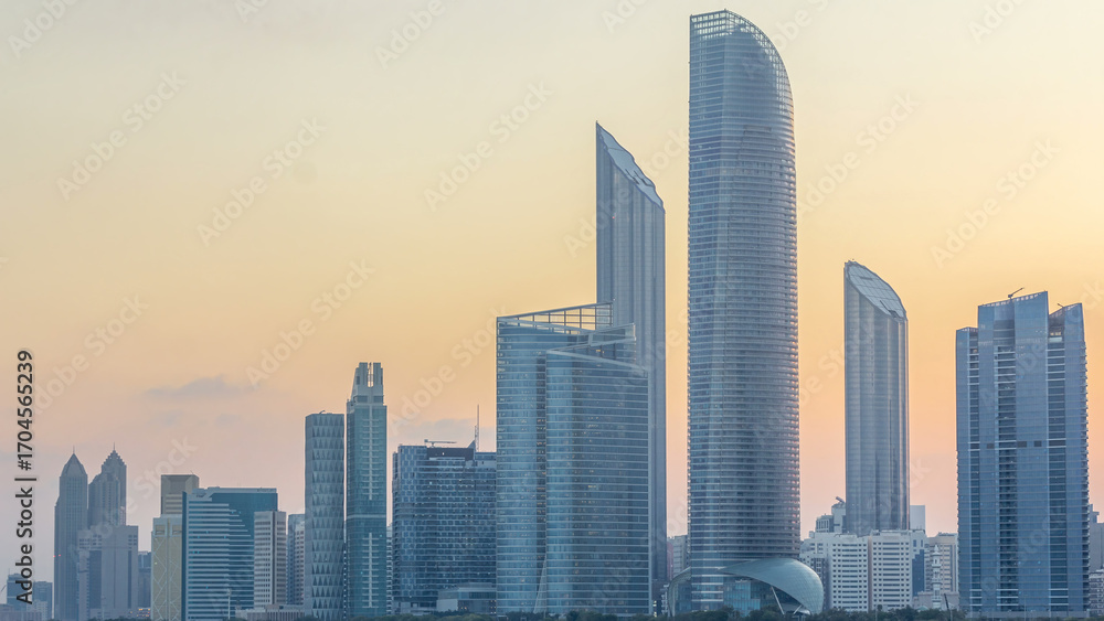 Fototapeta premium Abu Dhabi city skyline with skyscrapers before sunrise with water reflection night to day timelapse