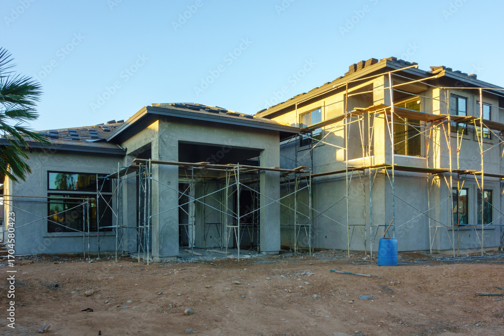 Obraz premium Construction of modern residential buildings with scaffolding surrounding much of their exterior in early morning light.