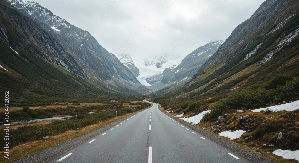 Naklejka premium Serene mountain road winding through a lush green valley, leading towards a distant glacier under a cloudy sky, ideal for travel and nature enthusiasts