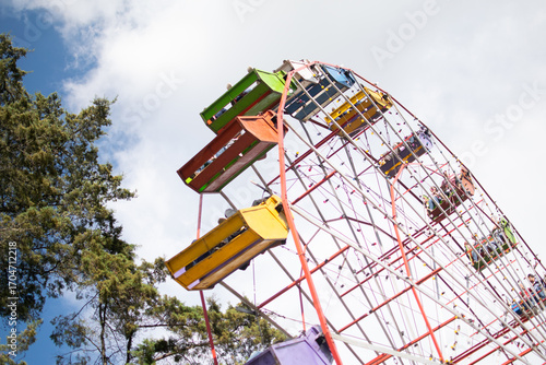 Photograph of a color wheel, a handmade mechanical ride in Central America, with people sitting in the chairs.