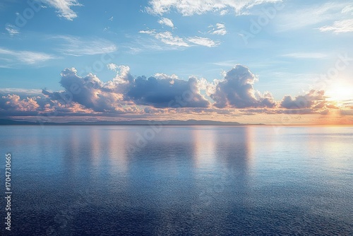 Calm sea under a cloudy sky at sunset with distant land on the horizon reflecting soft pastel colors on peaceful water