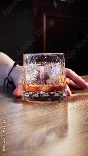 Ice cube dropped into a whiskey glass on a wooden bar