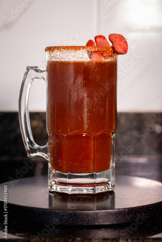 Mexican michelada drink is garnished with chili powder and tamarind candy, sitting on a black coaster