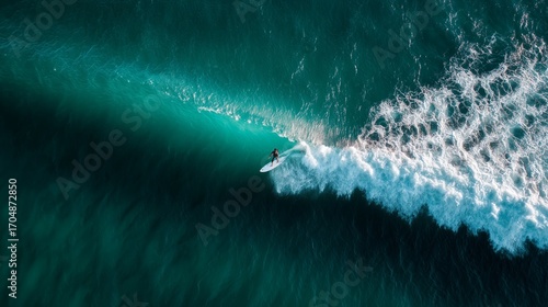 High-angle shot of a surfer skillfully riding a powerful wave in vibrant turquoise ocean waters, showcasing surfing excitement.