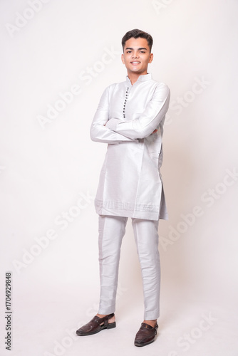 Young indian man wearing ethnic attire or kurta outfit standing isolated on white studio background. Asian Fashion model looking at camera. India.