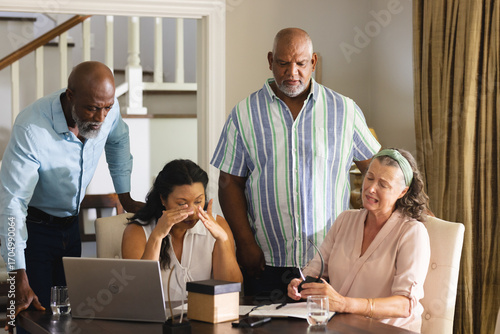 Discussing finances at home, senior group looking concerned around laptop and documents
