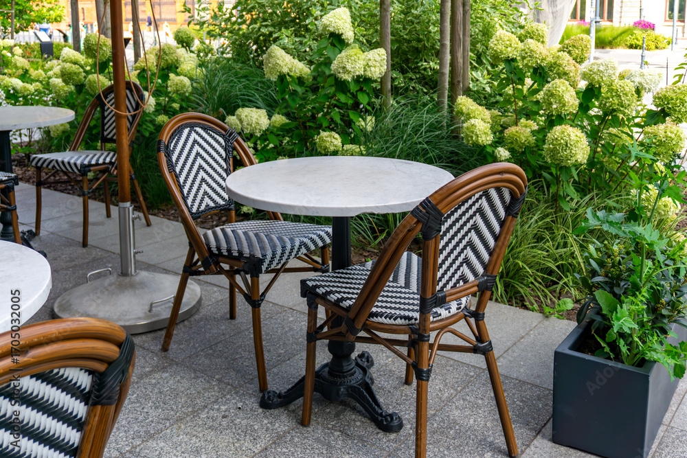 Fototapeta premium Restaurant garden in Łódź with round tables and woven chairs, surrounded by hydrangeas and decorative greenery.