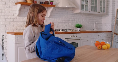 Happy elementary school kid getting ready for school in kitchen, packing backpack with books and supplies. Excited smiling child feeling confident and motivated before starting new day of learning.