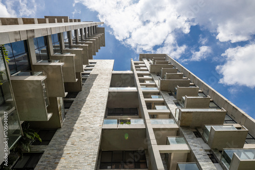 Fototapeta Striking upward shot of a high-rise building with concrete and stacked stone walls and alternating balconies