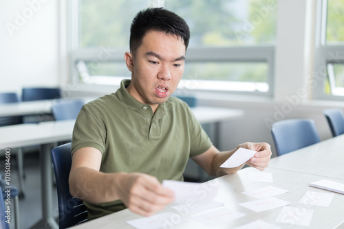 Young man using flashcards to study in a classroom. Concept of language learning or immigrant in ESL class.