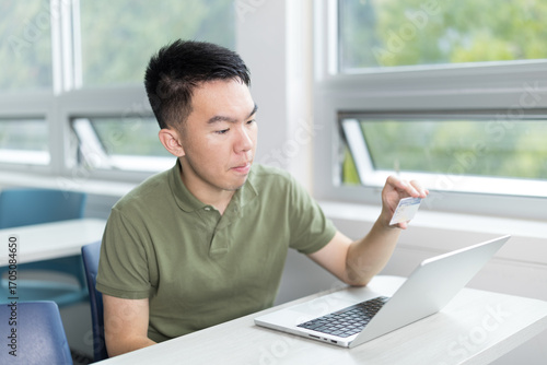 Young man holding up an ID card in front of a laptop, completing an online identification process.