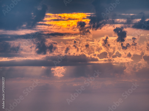 Stunning sunset sky with dramatic cloud formations glowing in shades of orange, purple, and blue. Atmospheric light rays create a magical evening mood, perfect for nature, travel, and scenic backgroun