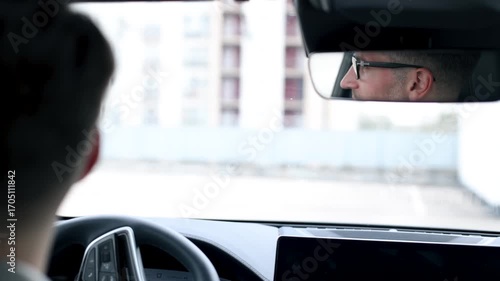 A man in glasses is looking into the rear view mirror of a car