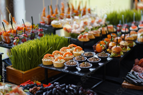 Variety of snacks on buffet table: shrimp tartlets, mini burgers, and vegetable canapés.