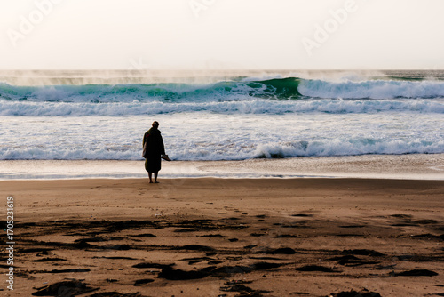Woman standing barefoot on the beach looking at ocean waves in Portugal