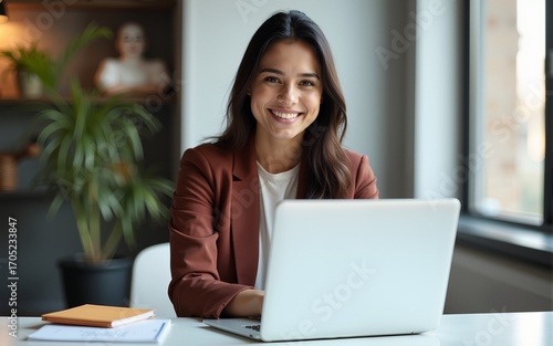 Vertical portrait of confident businesswoman leader in her 30s at work desk. Smiling Hispanic young woman entrepreneur, happy female executive manager looking at camera sitting at work with laptop.