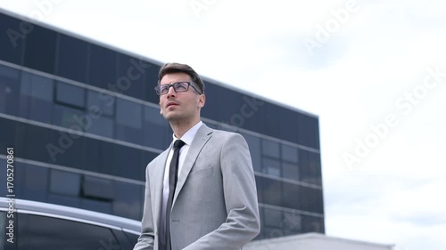A man in a suit and tie stands in front of a large building