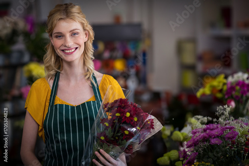 Florist holding wrapped yellow-centered red chrysanthemums amid shelves of vases, buckets, ribbons
