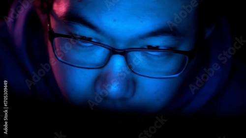 Close-up of a face in glasses, lit with blue and pink in the darkness