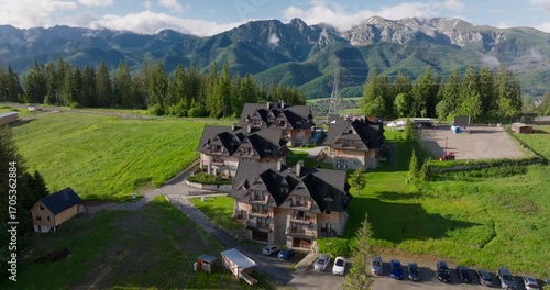 Aerial view of wooden mountain chalets on Gubałówka Hill in Zakopane, Poland, with the scenic Tatra Mountains in the background, a popular spot for tourism.