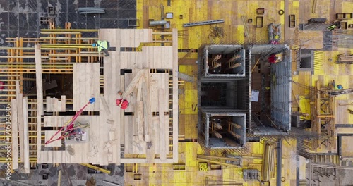 Top-down aerial shot of a residential building construction site, showing workers, wooden formwork, steel reinforcements, and construction materials in an organized and active work environment.