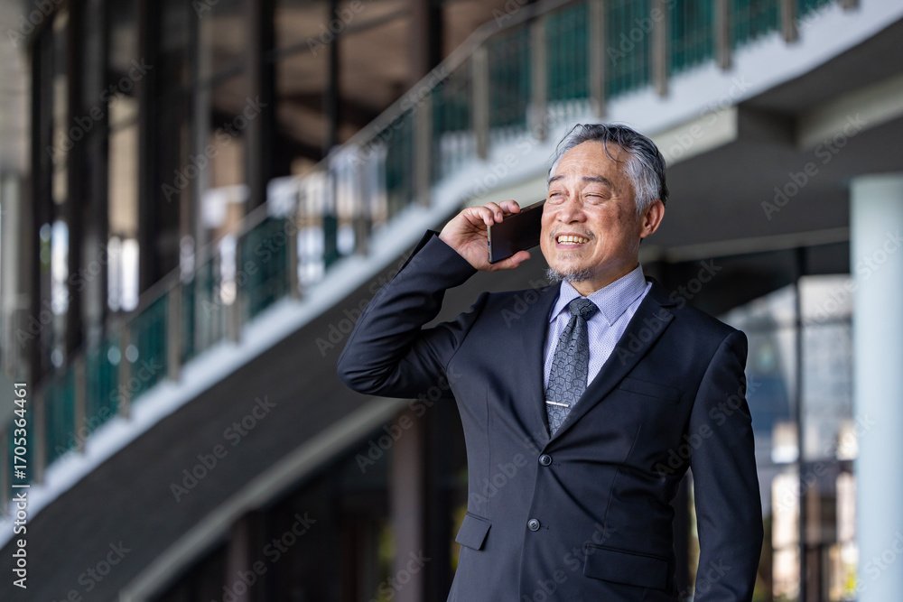 Senior business asian man is talking to mobile phone in his modern office for professional disscussion usage Senior business asian man is talking to mobile phone in his modern office for professional disscussion usage