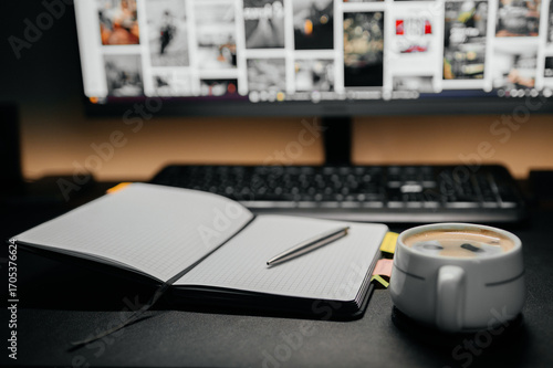 Open notebook with pen and coffee cup on desk near computer keyboard and monitor. Concept of remote work, studying, planning and productivity.