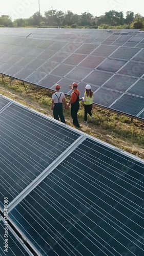 Engineers in safety gear inspect a solar panel array, emphasizing renewable energy and sustainable practices. Vertical video.
